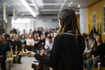 woman gives a public speech in front of 200 people, in an industrial environment