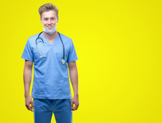 Wall Mural - Young handsome blond doctor with a happy face standing and smiling with a confident smile showing teeth