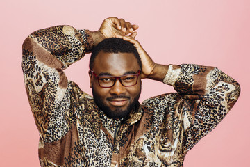 Wall Mural - Close up portrait of a man with glasses in leopard print shirt and arms up, isolated on pink studio background