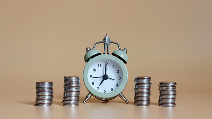 The piles of coins and a miniature businessman standing on an alarm clock.