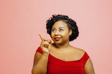 Young Woman In Red Dress Pointing And Looking Up, Isolated On Pink Studio Background