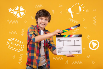 New film. Cheerful enthusiastic teenager standing with a clapstick in his hands and feeling excited while shooting his amateur film