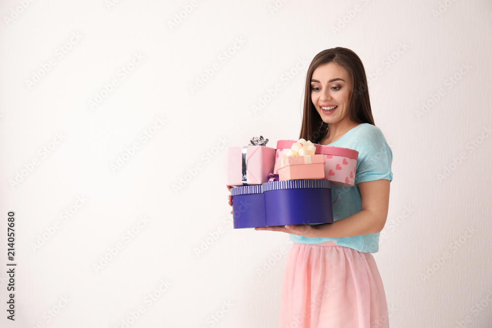 Beautiful young woman with gift boxes on light background