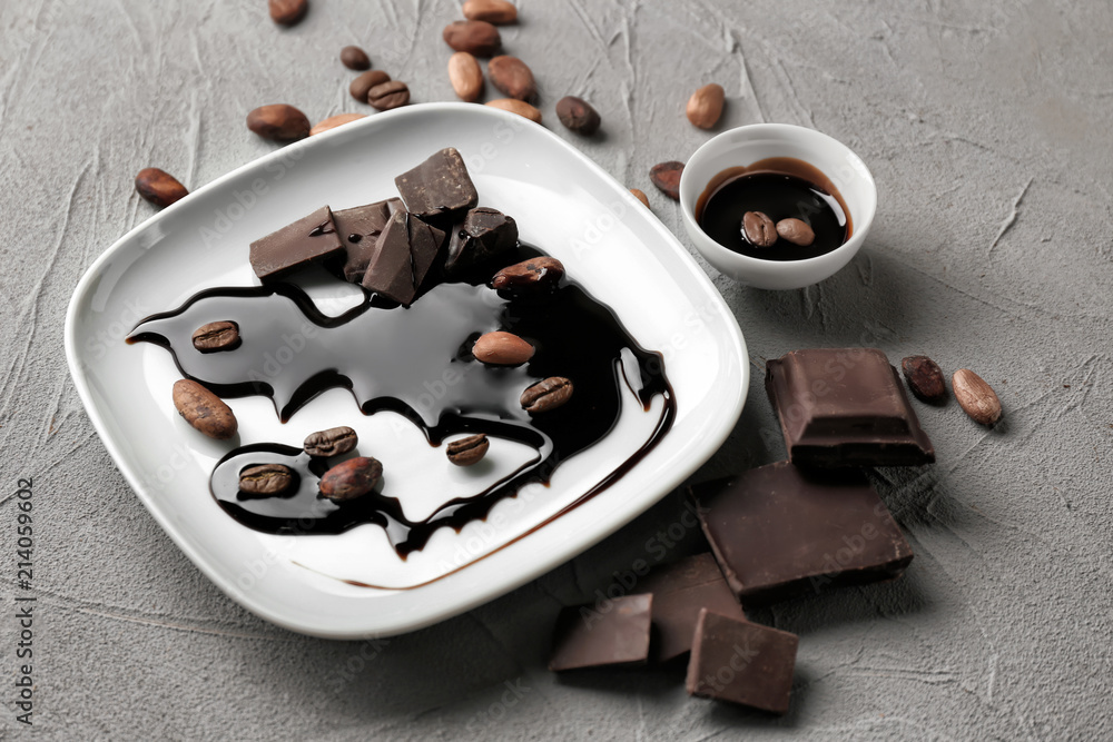 Plate with molten chocolate and cocoa beans on table