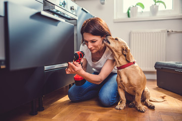 Wall Mural - Woman with dog building kitchen and using a cordless drill