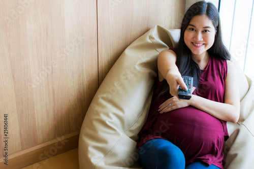 Happy Pregnant Woman Watching Tv Using A Remote Control And