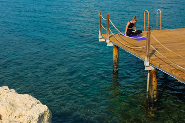 Wall Mural - Slim fit girl is practicing arm balance on wooden piece in the sea, person is very far, no face,  space for text