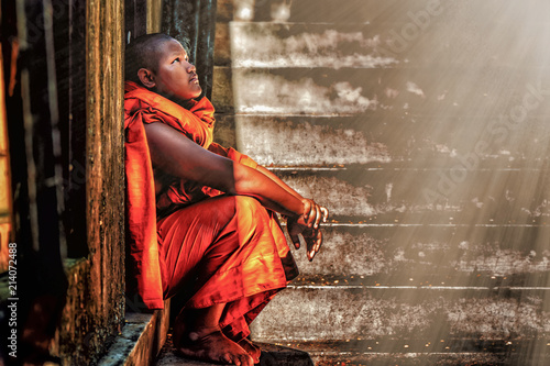 Cuadros en Lienzo A Thai Buddhist novice sitting at old temple door close to stair steps looking u