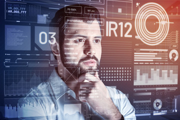 Standing and thinking. Calm clever experienced programmer thoughtfully looking at the information on the screen and touching his beard