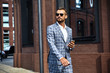 © halayalex - Portrait of sexy handsome fashion businessman model dressed in elegant checkered suit having business mobile conversation on smartphone on street. Metrosexual walking