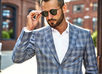 Portrait of sexy handsome fashion businessman model dressed in elegant checkered suit posing on street background. Metrosexual