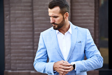 Portrait of sexy handsome fashion businessman model dressed in elegant blue suit posing on street background. Metrosexual