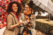 © BalanceFormCreative - Two female best friend walks at the city street with umbrellas above head.They smiling and making fun.Raining day and autumn concept.