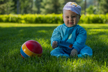 baby sitting on the soft grass in the city Park with his colorful ball