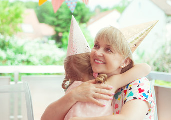 Wall Mural - Portrait of happy grandmother hug her granddaughter at her birthday party on terrace