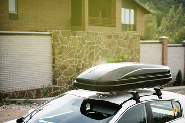 roof of the car with a black cargo box on the hooks near the country house in the evening.