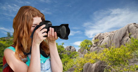 Wall Mural - travel, tourism and photography concept - happy young woman with backpack and camera photographing over background of seychelles island beach in indian ocean