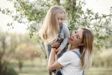 young mother with adorable daughter in park with blossom tree