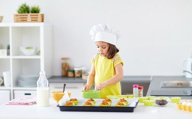 Wall Mural - family, cooking, baking and people concept - little girl in chefs toque making batter for muffins or cupcakes at home kitchen