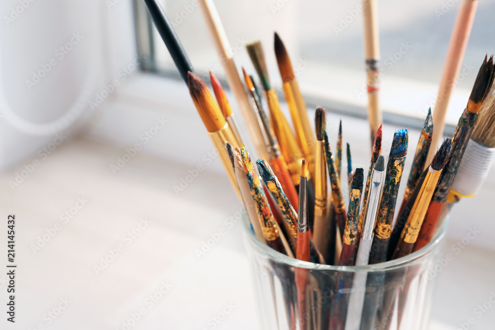 Glass with painting brushes on window sill, closeup
