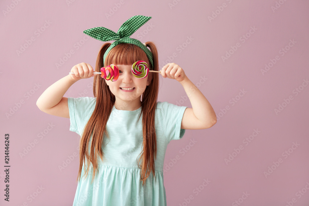 Cute little girl with lollipops on color background