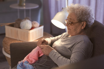 Wall Mural - Senior woman knitting warm sweater in armchair at home