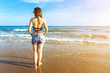 Back view of asian woman wearing biniki with short jeans and bright sunglasses posing at the beach having enjoy on vacation in tropical country