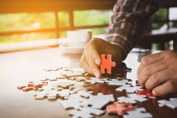 Hand holding piece of blank jigsaw puzzle on wooden table background.