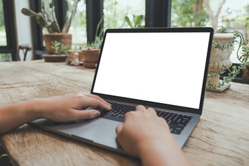 Mockup image of hands using and typing on laptop with blank white desktop screen on vintage wooden table in cafe