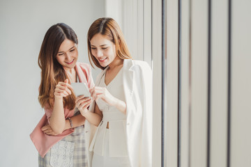 Wall Mural - Two young asian business woman in suit using smart phone for online shopping, internet banking and buying service from the internet.