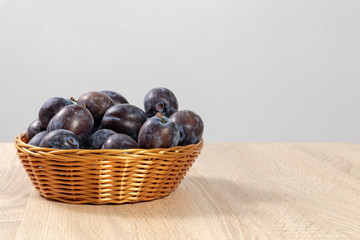 Sticker - Front view of a basket full of ripe plums on a wooden table