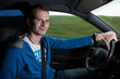 Junger männlicher Autofahrer lächelnd mit der Hand am Lenkrad
