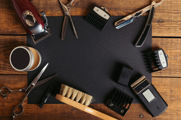 Top view of various professional barber tools on black card on wooden surface