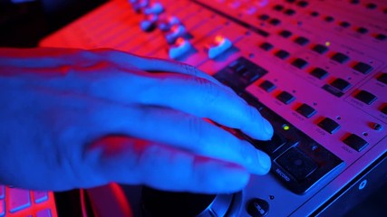 Wall Mural - Sound engineer rotates the scroll wheel on mixing console in a professional recording studio. Musician working on new song. Slow motion. 4k. Neon light.