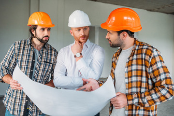 Wall Mural - group of handsome architects with blueprint having conversation inside of constructing building