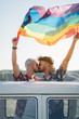 © ADDICTIVE STOCK - Couple kissing while holding rainbow flag in van