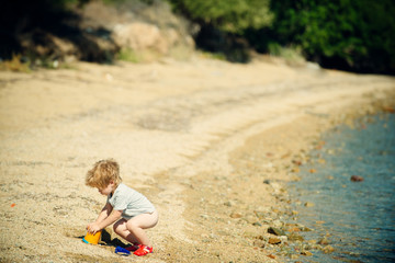 Child on the beach. A little boy is playing with sand near the sea on vacation. Space for text. Summer vacation, tourism, travel to the ocean. Warm summer near the water on the beach