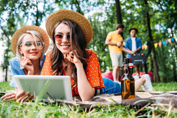 beautiful women using tablet while multiethnic men cooking food on grill behind