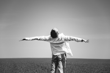 Black and white photos. A young guy is standing in the field with arms outstretched, his back to the camera.