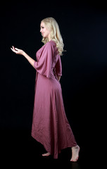 Wall Mural - full length portrait of blonde girl wearing long purple dress. standing pose. black studio background.