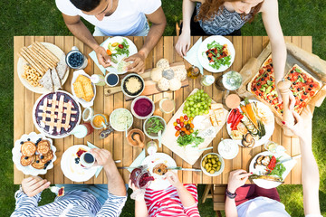 Wall Mural - Top view on wooden table with pastry, pizza and fruits during garden party