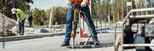 Fotografía Builder drilling the road with a tool and his coworker at the city road work con