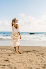 Wall Mural - Pretty girl in casual clothes and wooden sunglasses stay on the hot sand. Beautiful lady on sea exotic beach sunset or ocean sunrise. Travel, explore, active yoga and meditation lifestyle concept.