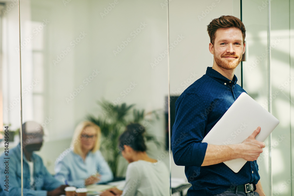 Smiling young businessman standing with his laptop in an office Stock ...