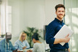 © Flamingo Images - Smiling young businessman standing with his laptop in an office