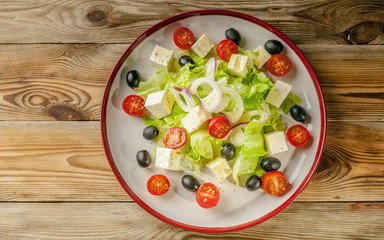 Greek salad with feta cheese, cherry tomatoes and olives in a round plate on a wooden background. Summer menu. Top view