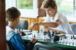 © Natali - cute handsome boy in white tshirt plays chess with his rival in chess class. Education concept, intellectual game. Chess tournament, lesson, camp, training concept