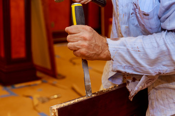 Man carpenter makes a hole in the wooden a door for a hammer and chisel.