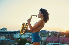 Young Girl With Saxophone On The Roof Parapet. Woman Holding A Musical Wind Instrument. Young Musician Looking For Inspiration