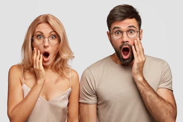 Wall Mural - Studio shot of shocked wife and husband find out they will become grandparents very early, keep jaws dropped, stand closely together against white background. People, reaction, relationship concept